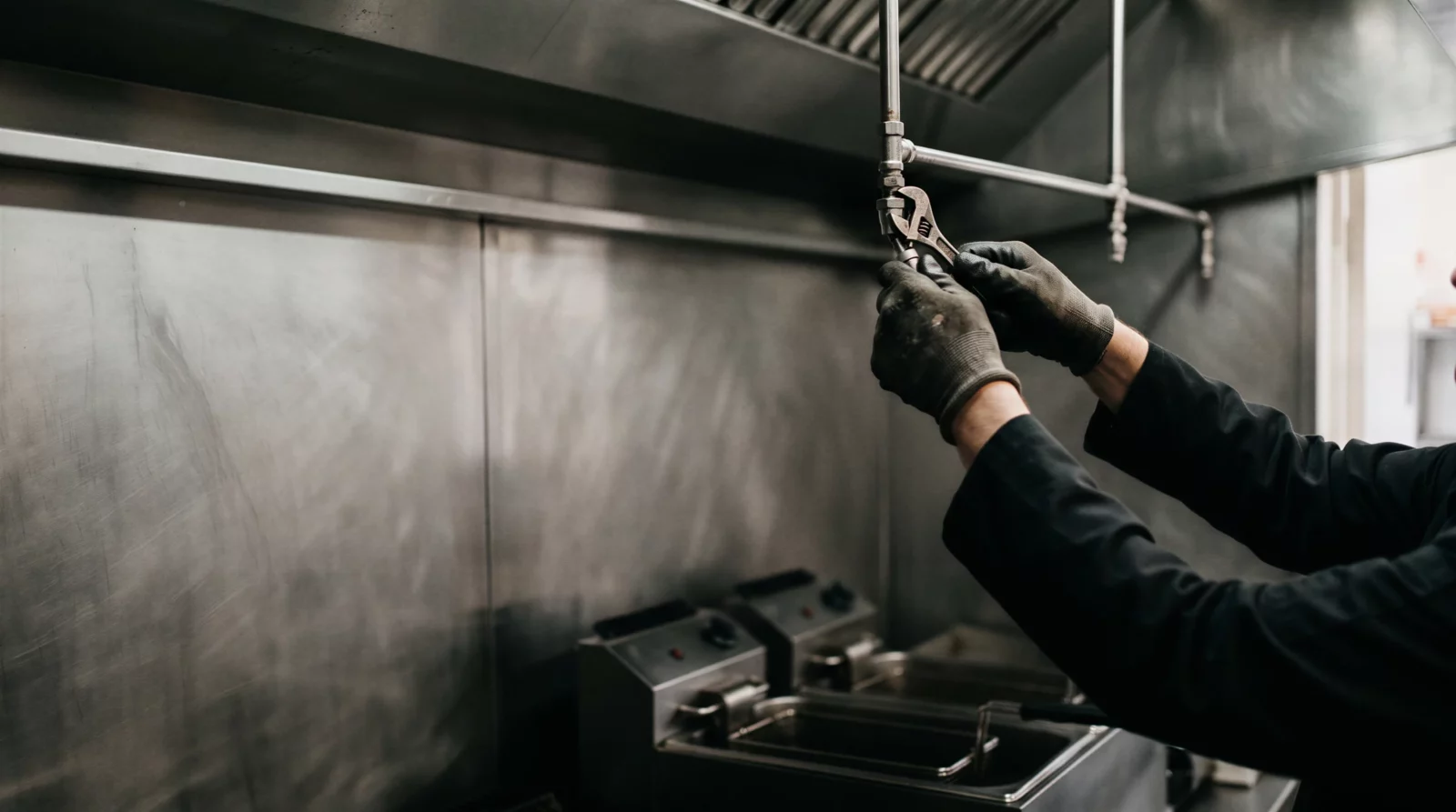 Technicien qui serre une buse de diffusion sur le réseau d'une hotte de cuisine professionnelle, au-dessus des friteuses