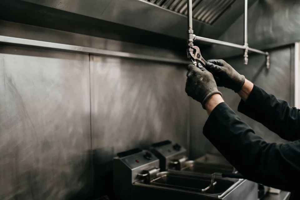 Technicien qui serre une buse de diffusion sur le réseau d'une hotte de cuisine professionnelle, au-dessus des friteuses