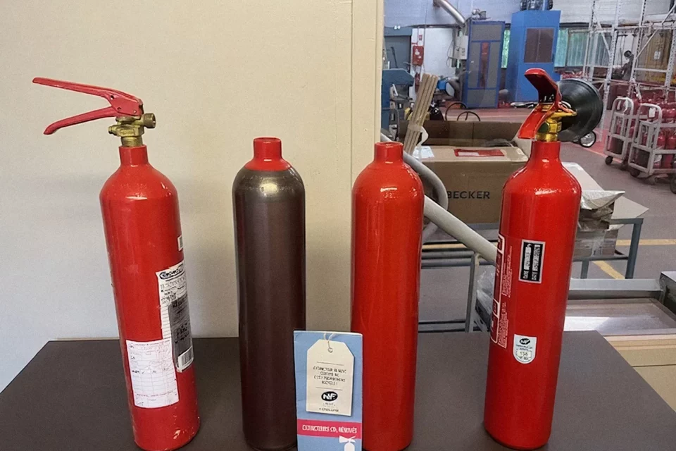 Étapes de la rénovation d'un extincteur CO2 : appareil usagé, bouteille décapée, bouteille repeinte, extincteur rénové