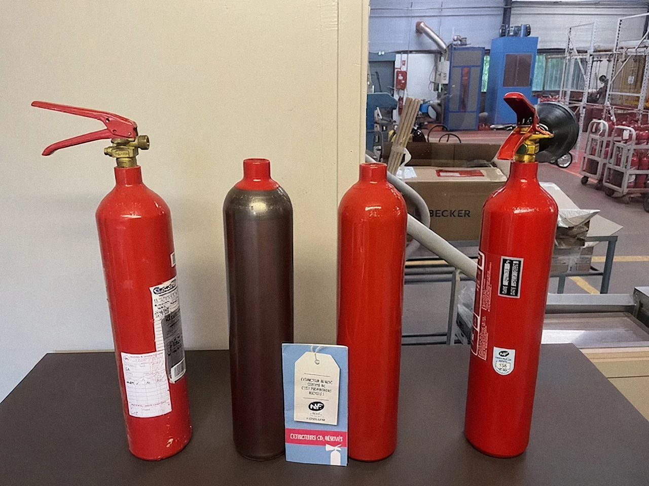 Étapes de la rénovation d'un extincteur CO2 : appareil usagé, bouteille décapée, bouteille repeinte, extincteur rénové
